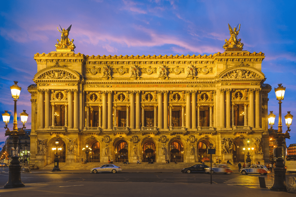 The ornate facade of the Palais Garnier opera house lit up at dusk