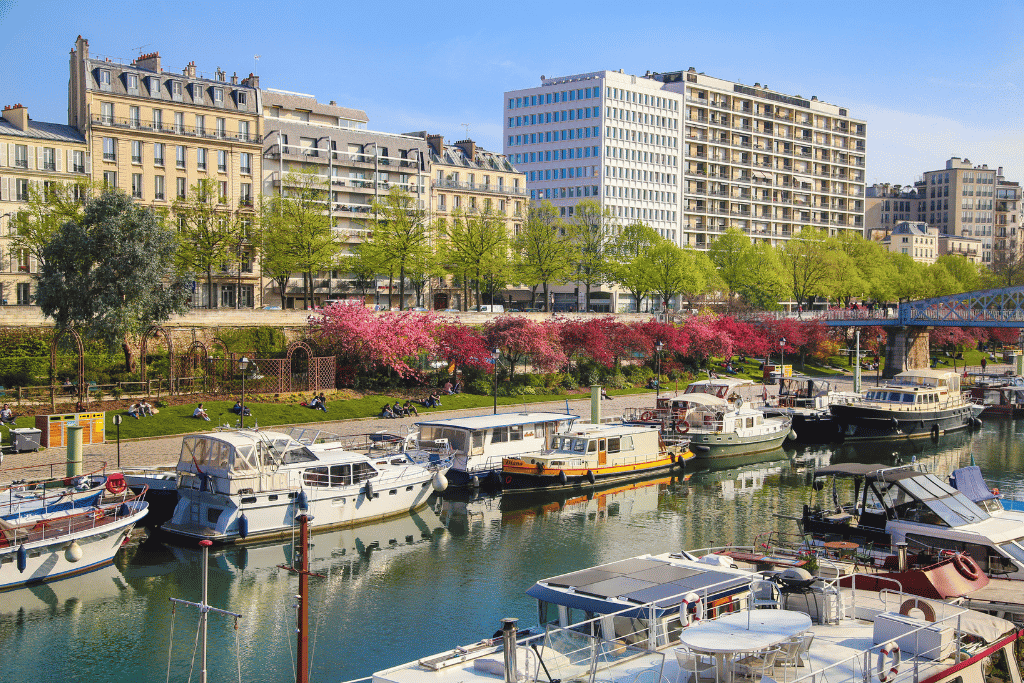 Houseboats moored along Canal Saint-Martin with cherry blossom trees lining the bank
