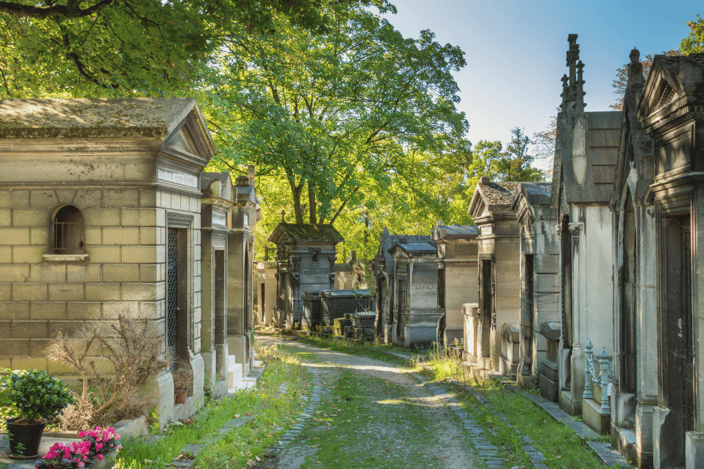 A tree-shaded gravel path between stone mausoleums in Père Lachaise Cemetery