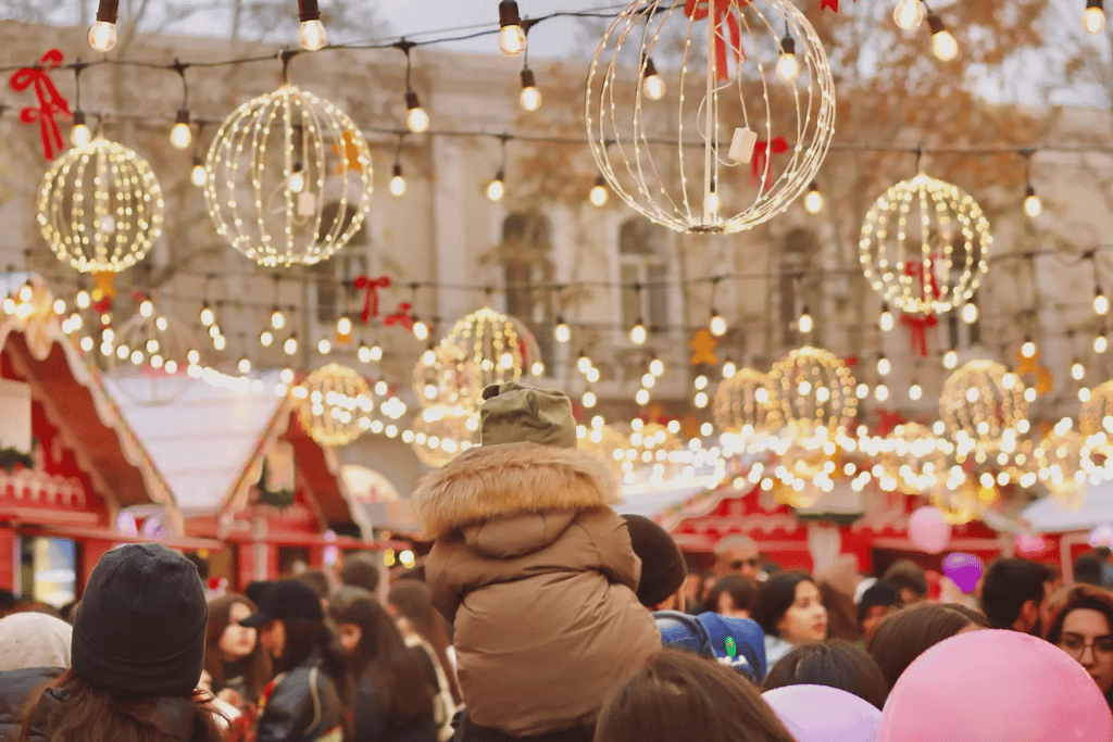 Illuminated ornament-shaped lights strung over a crowded Paris Christmas market
