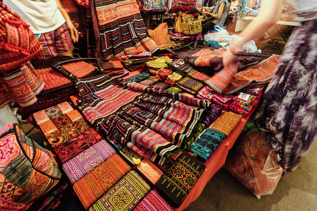 A market table piled with colourful embroidered hill-tribe bags and textiles at the Night Bazaar