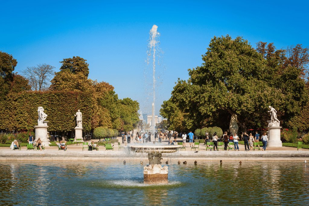 The central fountain in the Jardin des Tuileries with statues and visitors relaxing on green chairs