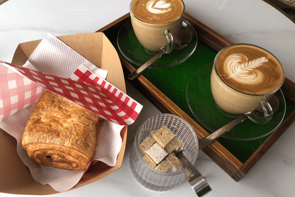 A flaky croissant beside two latte-art coffees on a café table