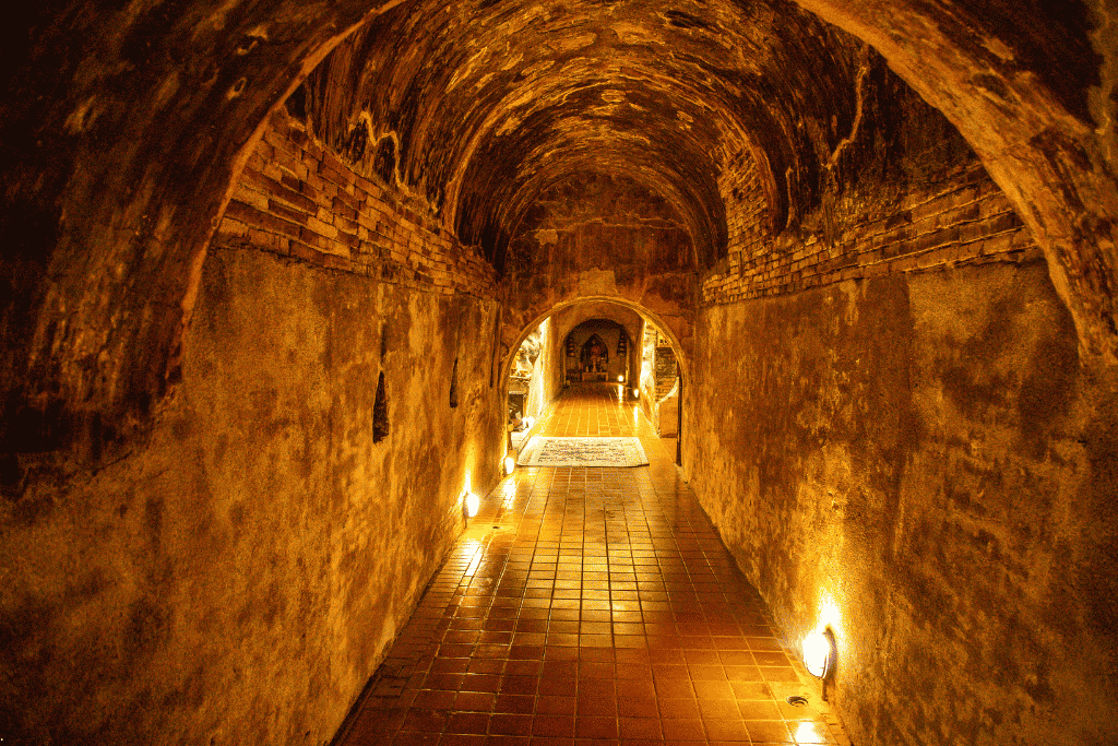 A softly lit brick meditation tunnel leading to a Buddha shrine at Wat Umong