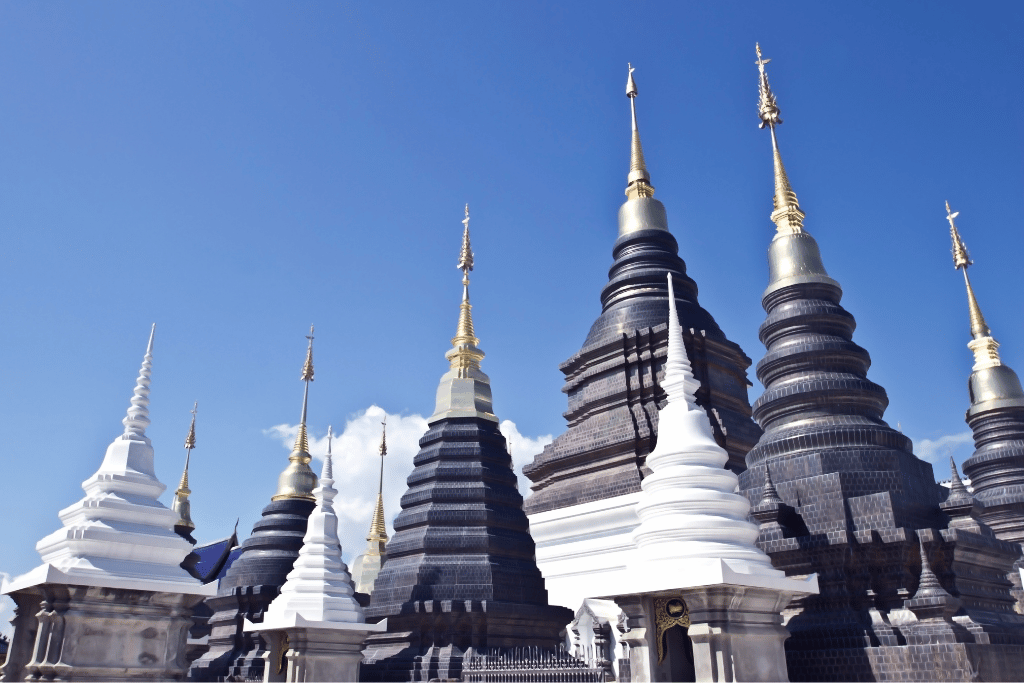 A cluster of ornate black-and-white stupas with golden tips against a blue sky at Wat Ban Den