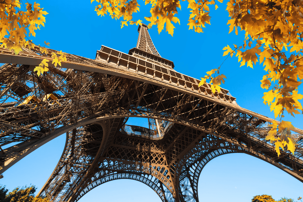 View looking up at the Eiffel Tower framed by golden autumn leaves against a blue sky