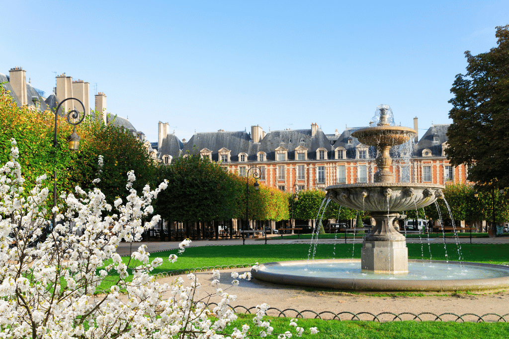 A fountain in Place des Vosges with the square's brick-and-stone buildings behind spring blossoms