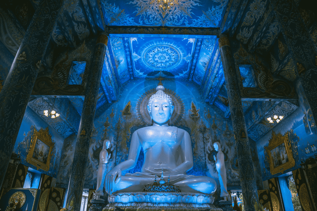 A white Buddha statue seated against vivid blue-and-gold painted walls inside Chiang Rai's Blue Temple