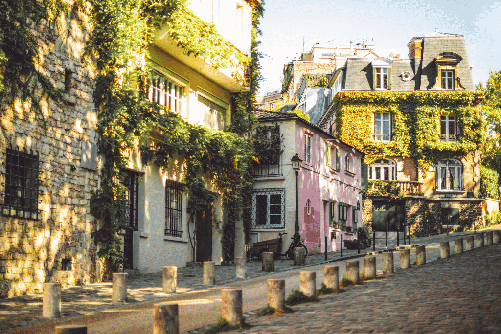 A quiet cobbled Montmartre street lined with ivy-covered buildings and a pink corner house