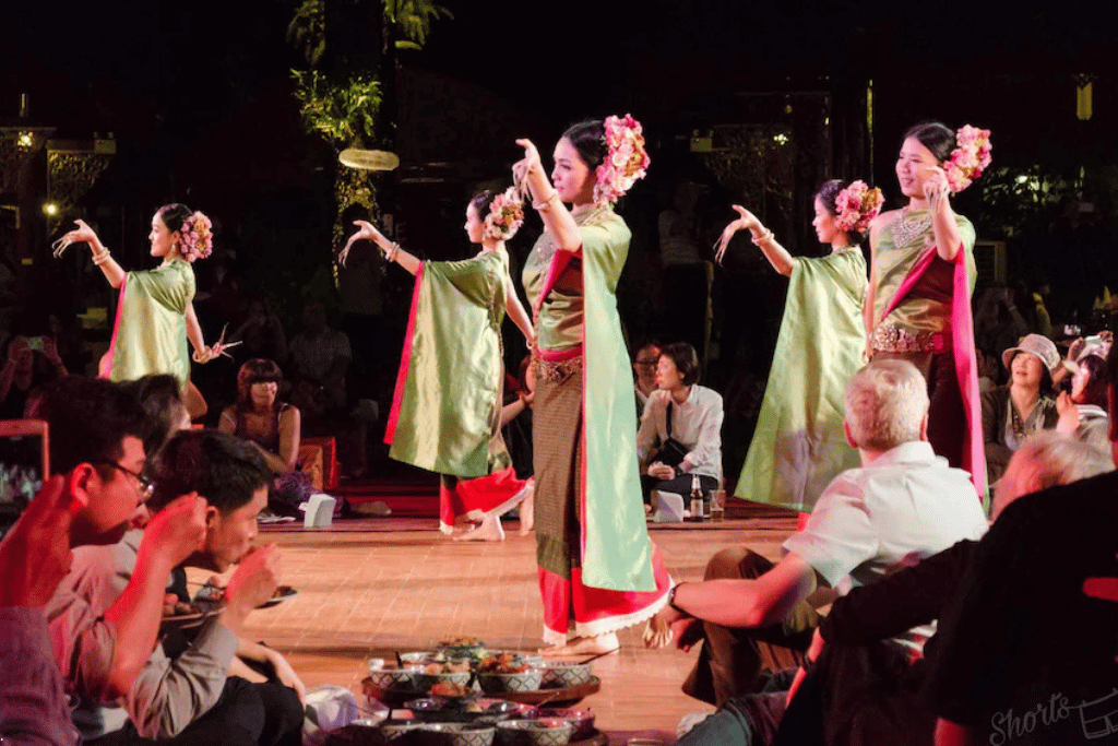 Dancers in green-and-red Lanna costumes performing for a seated audience at a khantoke dinner