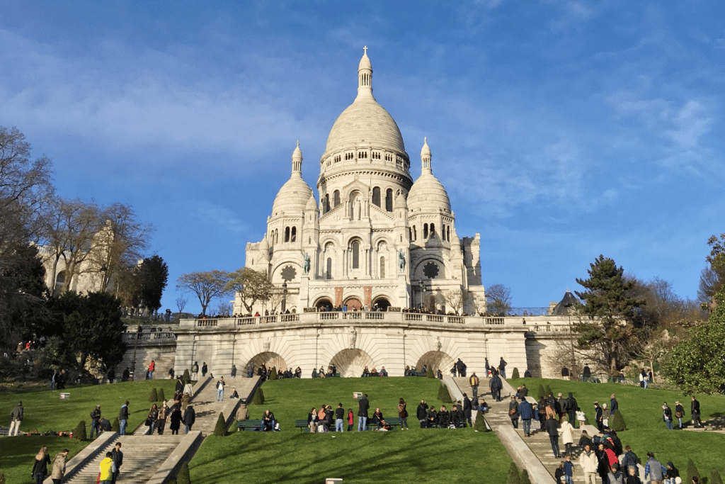 Sacré-Cœur basilica's white domes viewed from the lawns below, with visitors on the steps