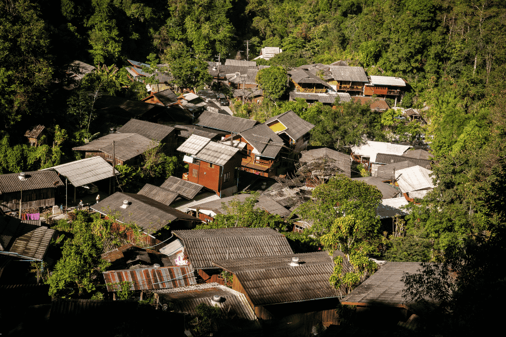 Wooden houses with tin roofs nestled in a dense green forested valley at Mae Kampong village