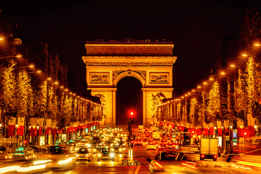 The Champs-Élysées lit up at night leading to the Arc de Triomphe, with traffic streaming past
