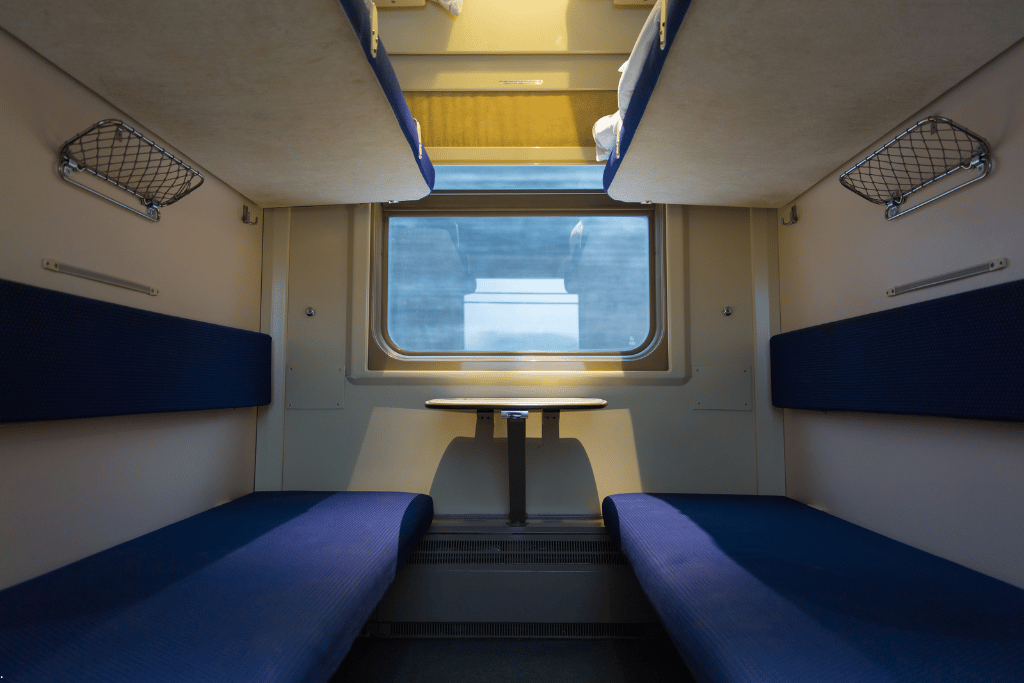The blue bench seats and window of an overnight sleeper train compartment
