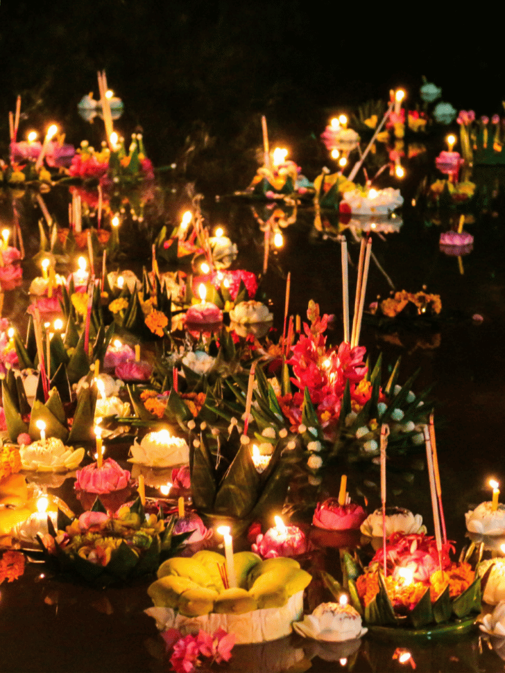 Candlelit krathong floats of banana leaves and flowers drifting on dark water at night