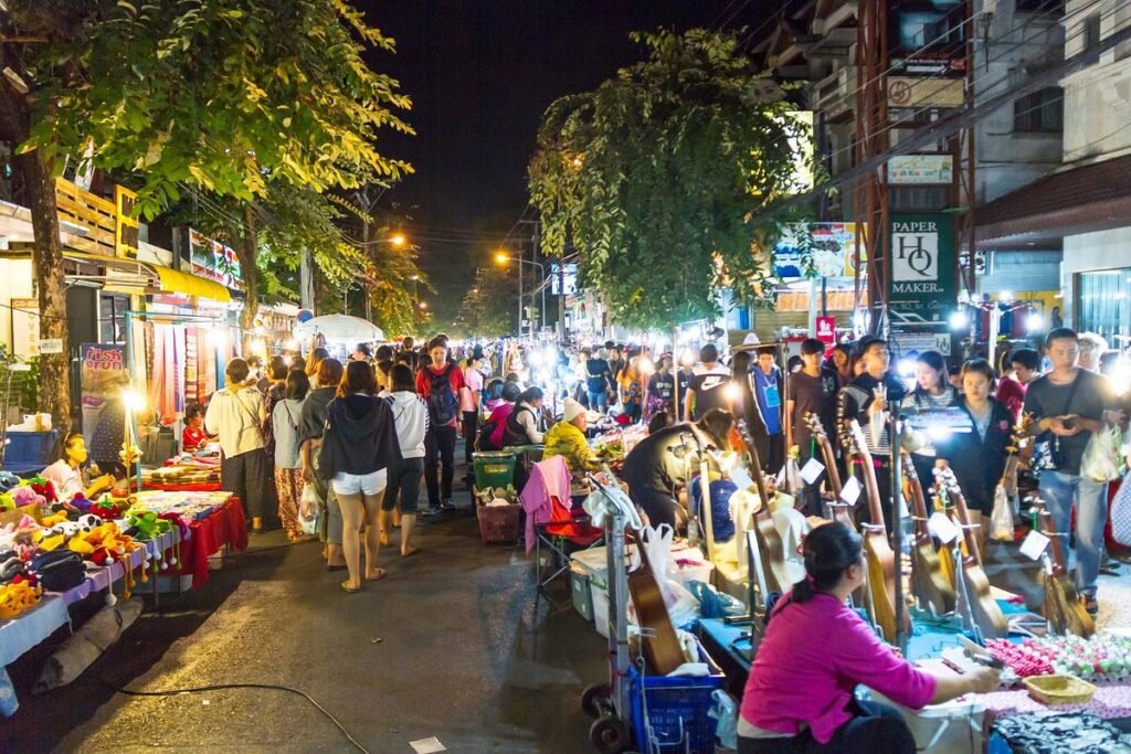 Crowds browsing lit stalls, including a handmade-instrument seller, at a Chiang Mai night market