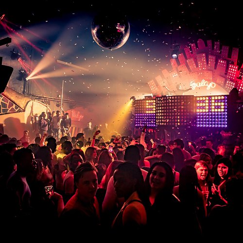 A crowded Paris nightclub dance floor with a disco ball and coloured lights overhead