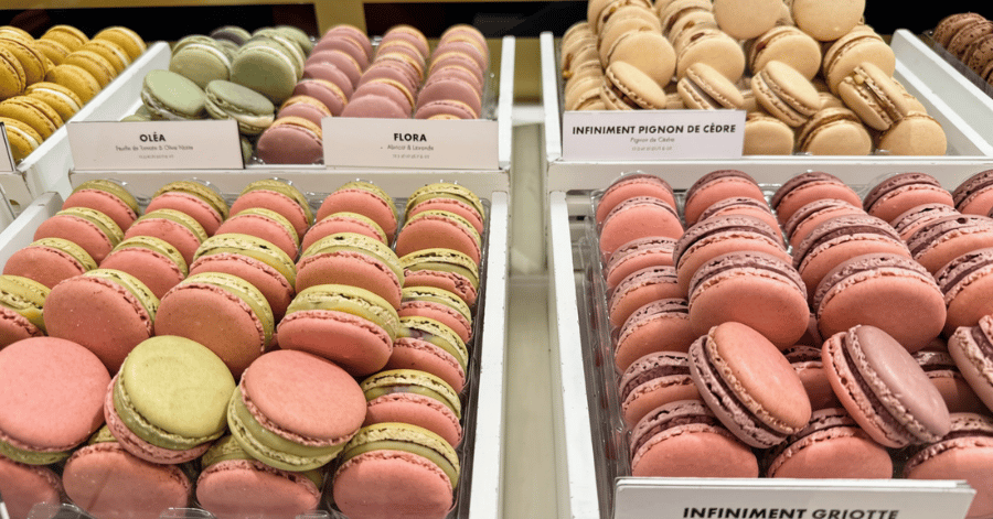 Rows of colourful macarons in flavours like Oléa and Infiniment Griotte in a Paris patisserie display case
