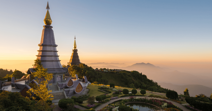 Two Lanna-style chedis on a mountaintop overlooking misty ranges at sunset in northern Thailand