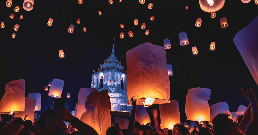 Glowing paper lanterns rising into the night sky above a lit temple during Chiang Mai's Yi Peng festival