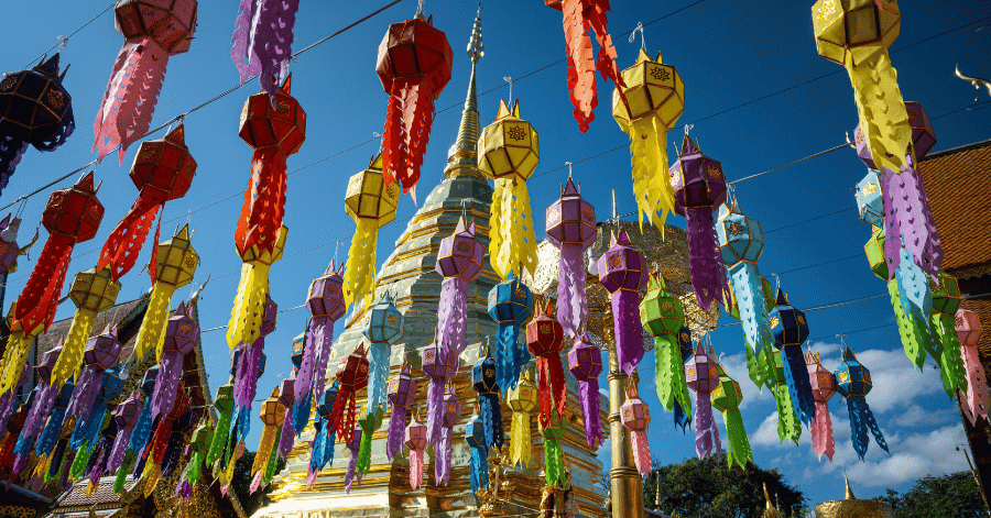 Colourful paper Lanna lanterns strung around a golden chedi against a blue sky in Chiang Mai