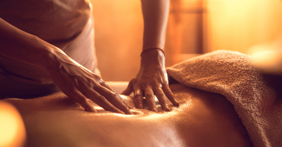 A therapist's hands pressing along a person's back during a Thai massage in warm light