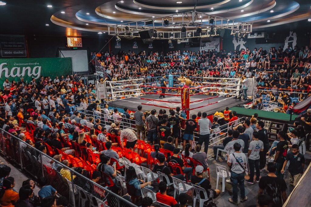 A fighter performing the wai kru in a boxing ring before a packed Muay Thai stadium crowd