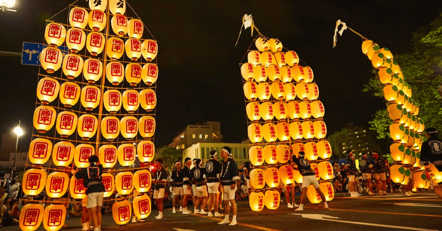 Tall bamboo poles strung with rows of glowing paper lanterns at a night festival