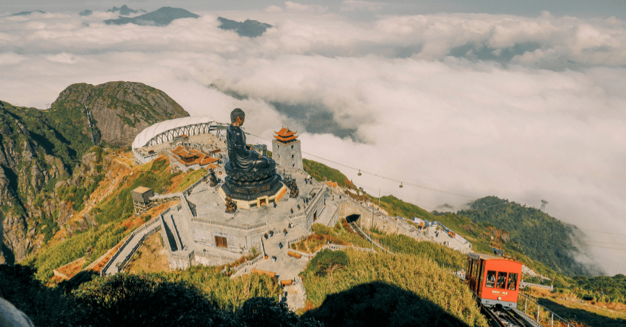 The Great Buddha statue and temples on the Fansipan summit above a sea of cloud, with the red funicular
