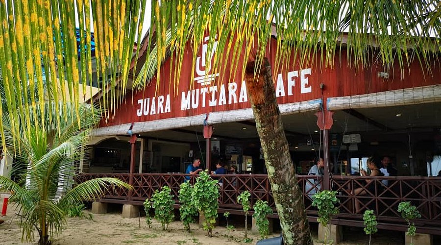 The beachfront exterior and sign of Juara Mutiara Cafe framed by palms