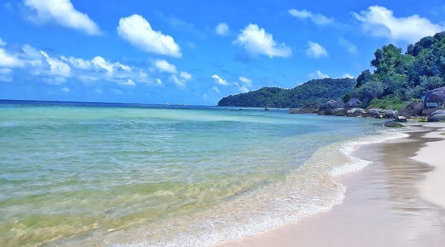 Clear turquoise shallows and soft white sand at Sao Beach, a forested headland beyond