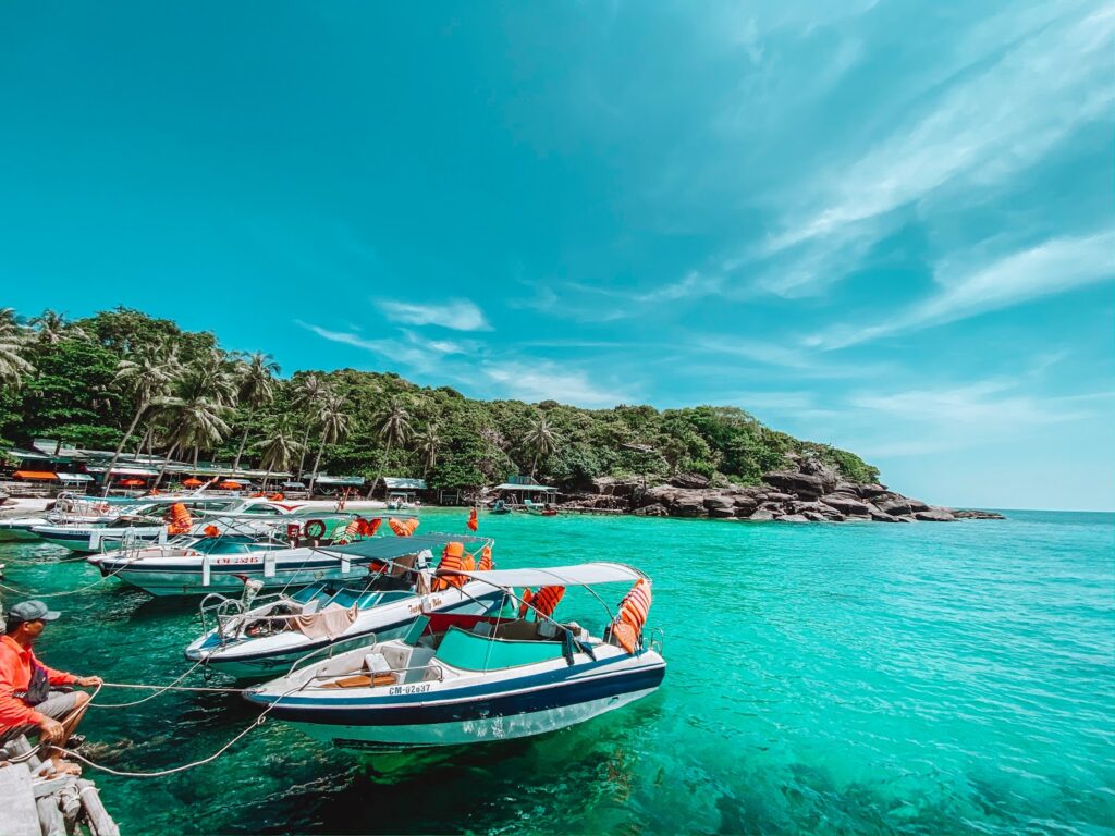 Speedboats moored in clear turquoise water by a palm-fringed, rocky Phu Quoc shore