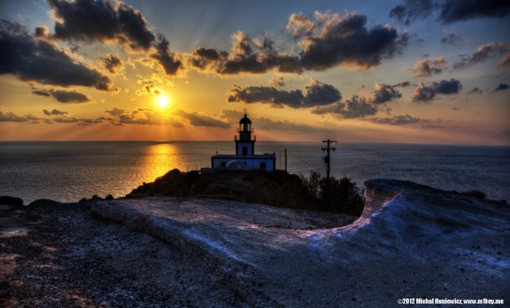 The Akrotiri Lighthouse on a headland silhouetted against the sun setting over the sea