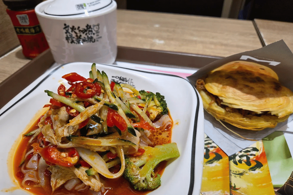 A plate of liangpi cold noodles in chilli sauce with vegetables and flatbread