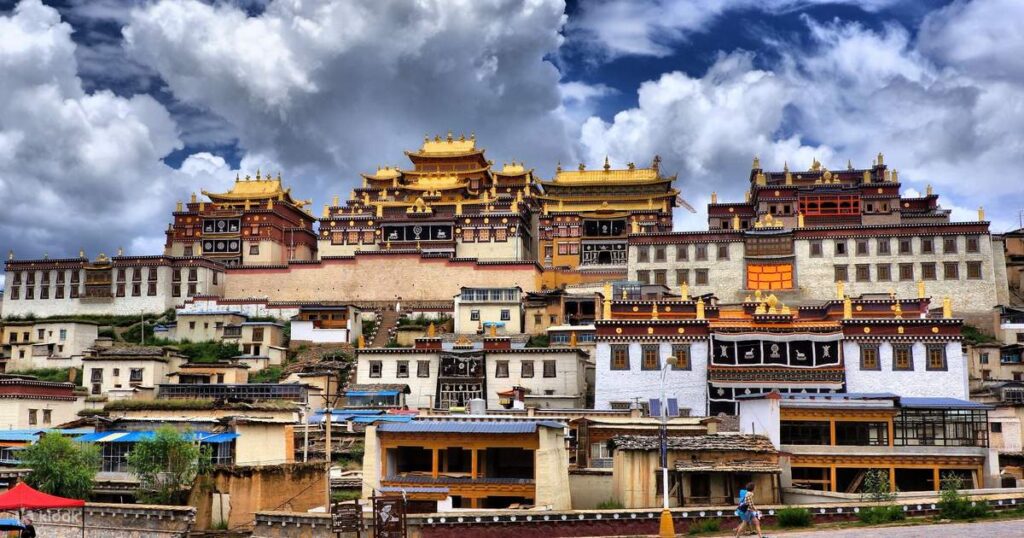 Golden-roofed white halls of Songzanlin Monastery climbing a hillside under dramatic clouds