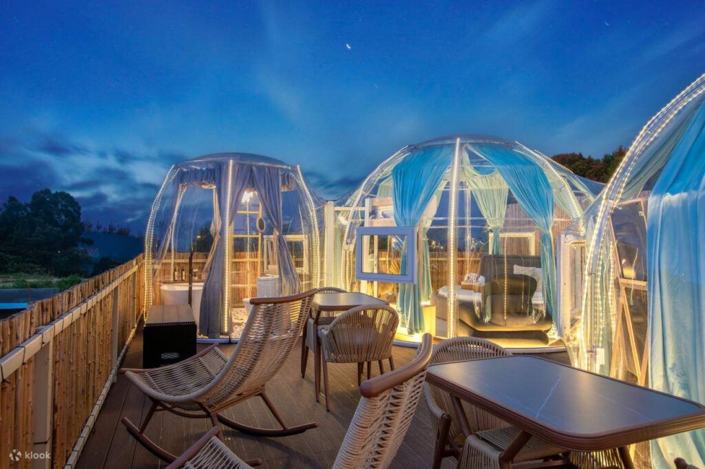 Illuminated transparent dome glamping tents on a timber deck at dusk in Cameron Highlands