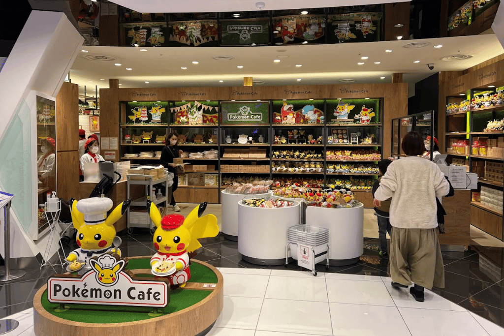 Pokémon Café entrance with a chef Pikachu statue beside the 'Pokémon Cafe' sign and seating beyond