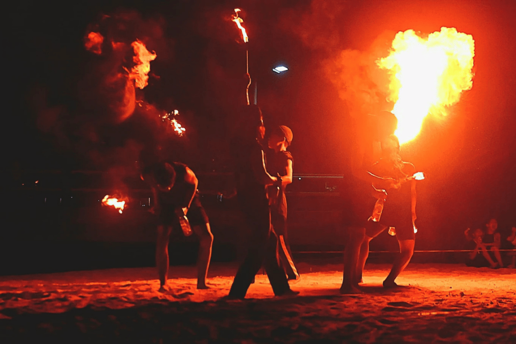 Performers spinning fire on a dark beach during a night fire show