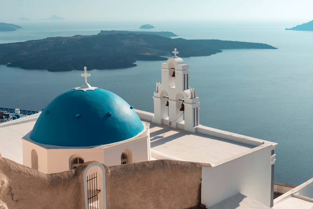 A blue-domed church and white bell tower overlooking the Santorini caldera and sea