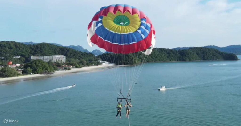 Two people parasailing under a colourful canopy over the sea near the coast