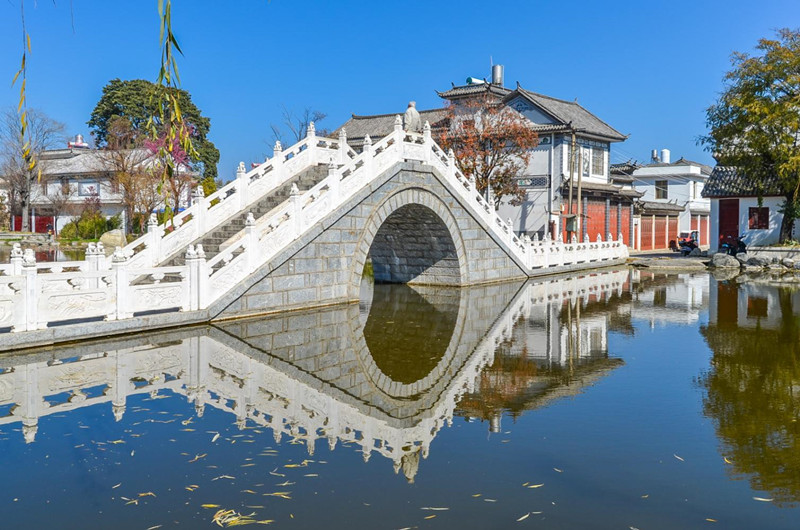 White stone arched bridge and traditional Bai houses reflected in a village pond, Dali