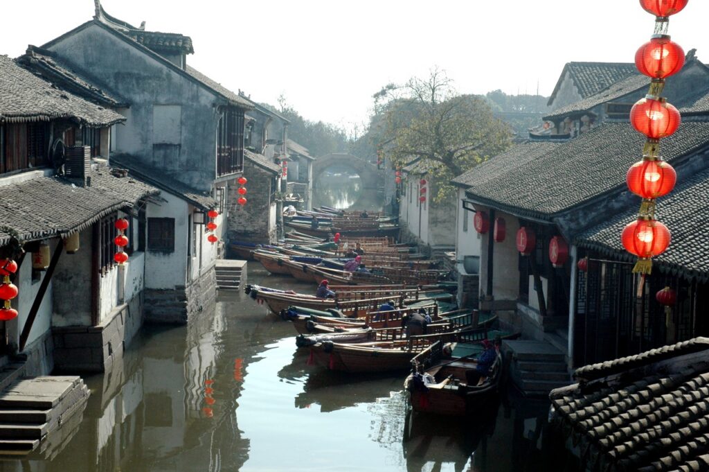 Wooden boats moored along a Zhouzhuang canal of old grey-tiled houses and red lanterns