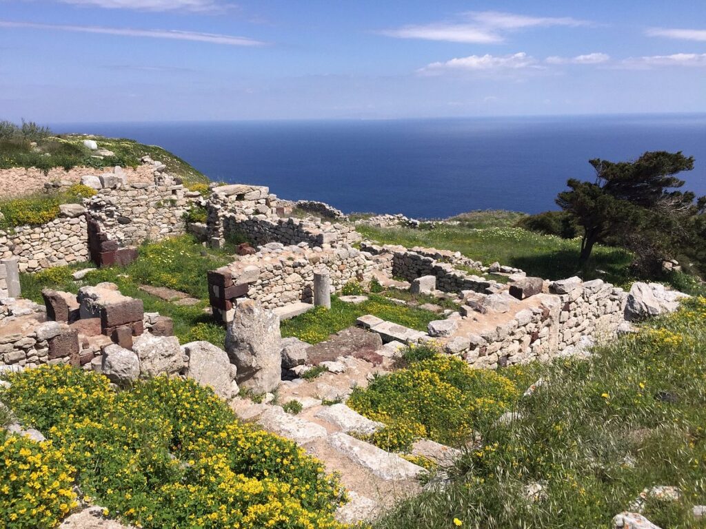 Ancient stone ruins among wildflowers on the Mesa Vouno headland above the sea, Santorini