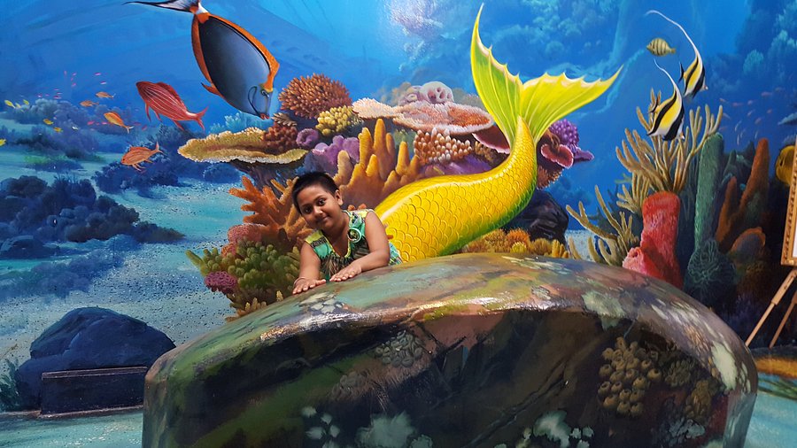 Child posing with a 3D underwater mermaid and coral reef mural