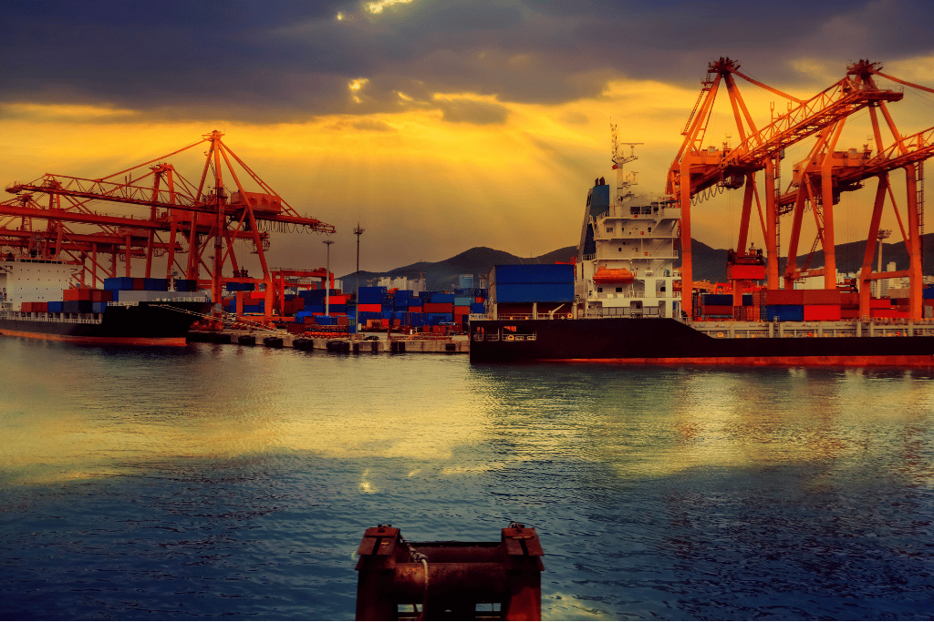 Container cranes and a cargo ship at Busan Port under a sunset sky