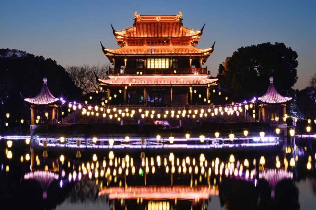 An illuminated tiered tower reflected in the water at Panmen Scenic Area at night