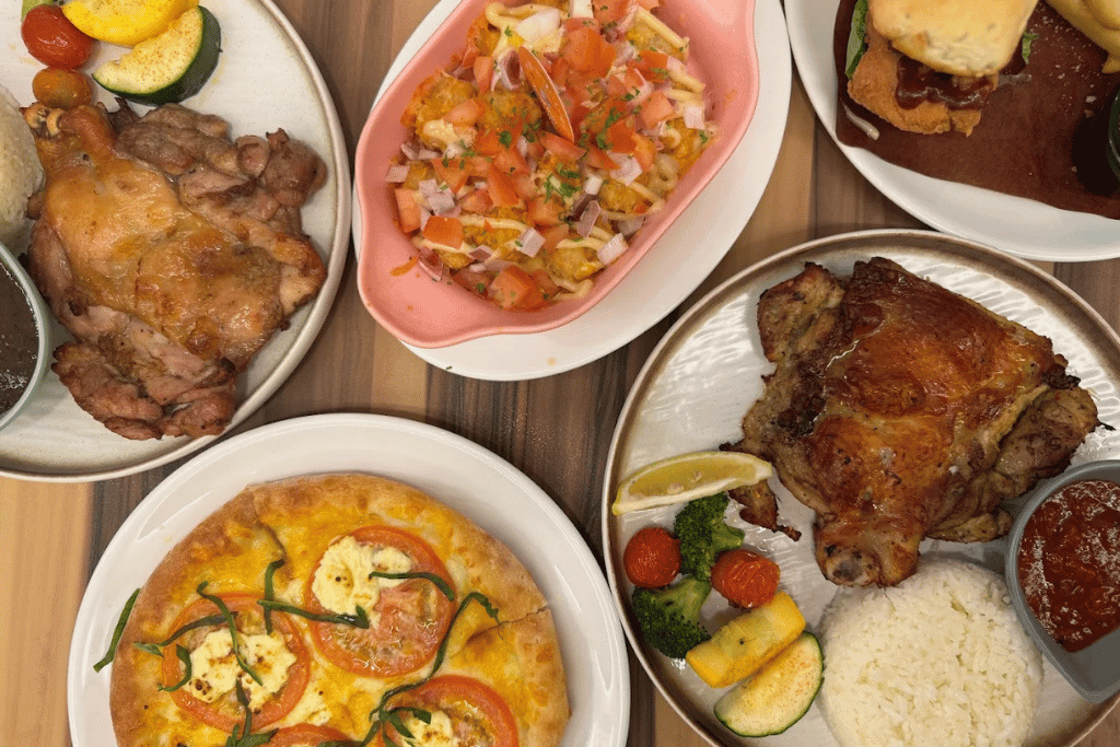 An overhead spread of fried chicken, rice plates, curry and salad on a wooden table in Desaru