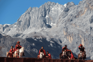 Performers on horseback in red Tibetan dress before the snow-capped Jade Dragon Snow Mountain