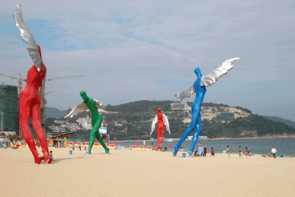 Colourful winged human sculptures standing on the sand at Dameisha Beach
