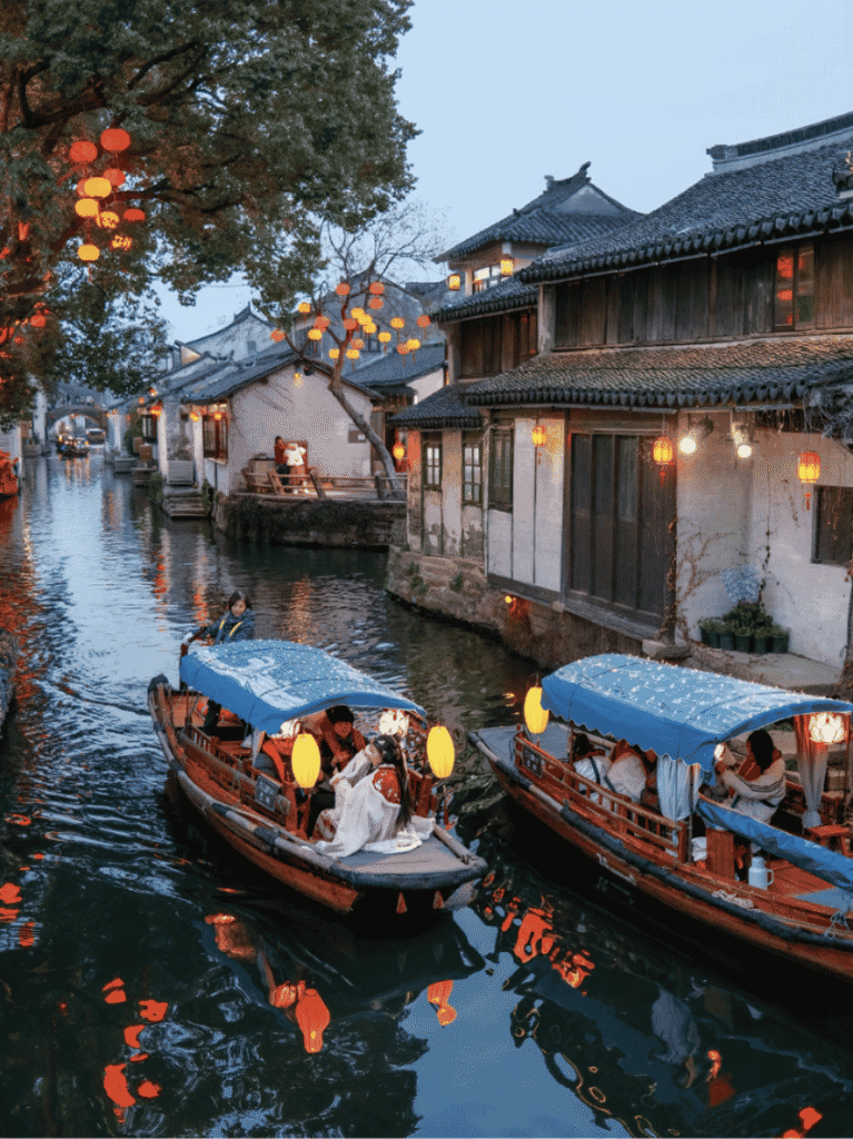 Wooden boats strung with red lanterns on a Suzhou canal at dusk